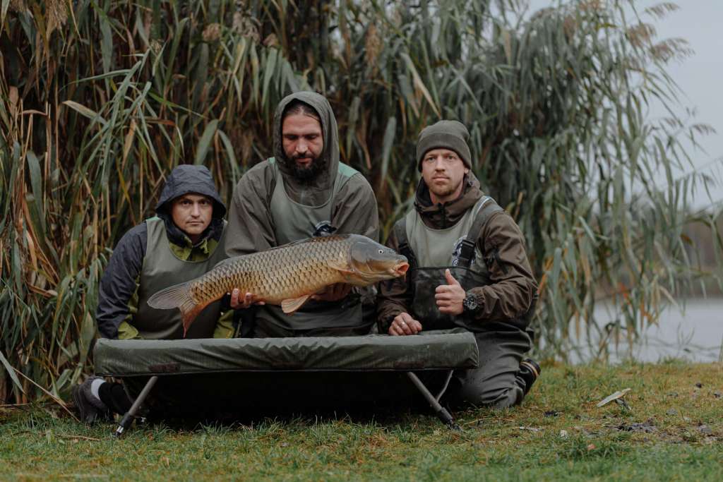 Three anglers posing together with a large catch near a lake.