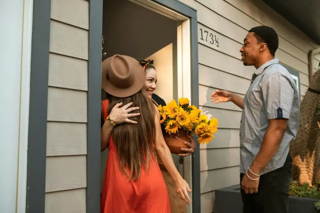 Guests warmly greet their vacation rental host with a bouquet of sunflowers at the door.