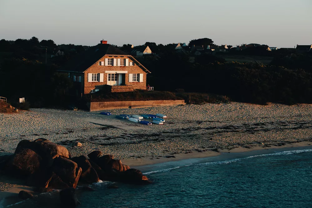 Cozy beachfront vacation rental house at sunset with small boats lined up on the sand.