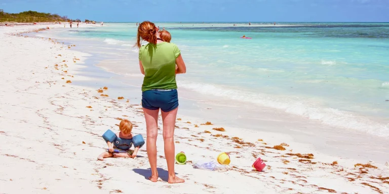 A girl holding a baby long the beach shoreline at one fo the 3 best beaches in the Florid Keys