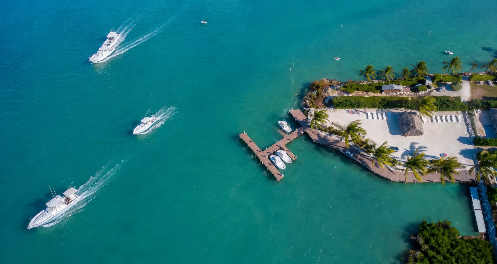Aerial view of luxury vacation rentals at Keys Cove in Marathon FL featuring private deep-water boat slips, boats cruising the channel, and a private sandy beach layout.